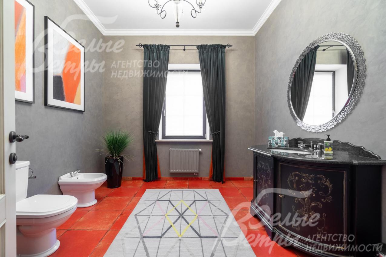 Санузел на первом этаже с насыщенным акцентным терракотово-красным полом, тумбой под раковину с изысканным орнаментом и картинами