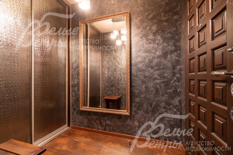 В прихожей находится большое зеркало в багетной раме с латунным оттенком и шкаф-купе с дверцами, украшенными текстурным рисунком