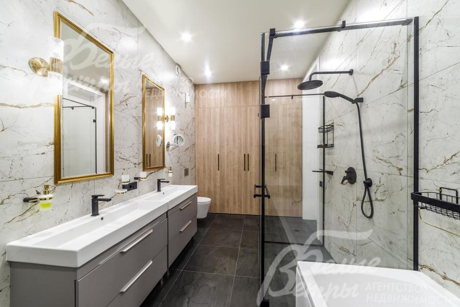Санузел при мастер-спальне с душевой и ванной. Стены облицованы плиткой под светлый мрамор с бежево‑серыми прожилками, пол — крупной тёмно‑серой плиткой с текстурой камня