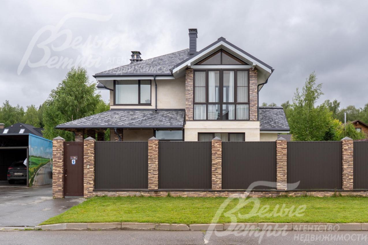 По фасаду дом ограждён забором с каменными столбами, облицованными искусственным камнем в стиле дома