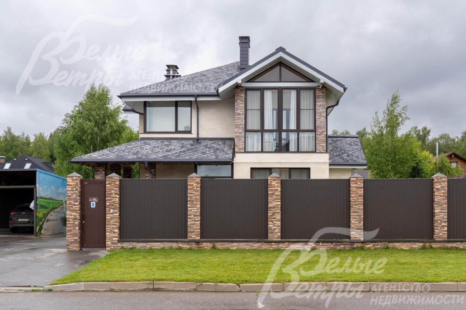 По фасаду дом ограждён забором с каменными столбами, облицованными искусственным камнем в стиле дома