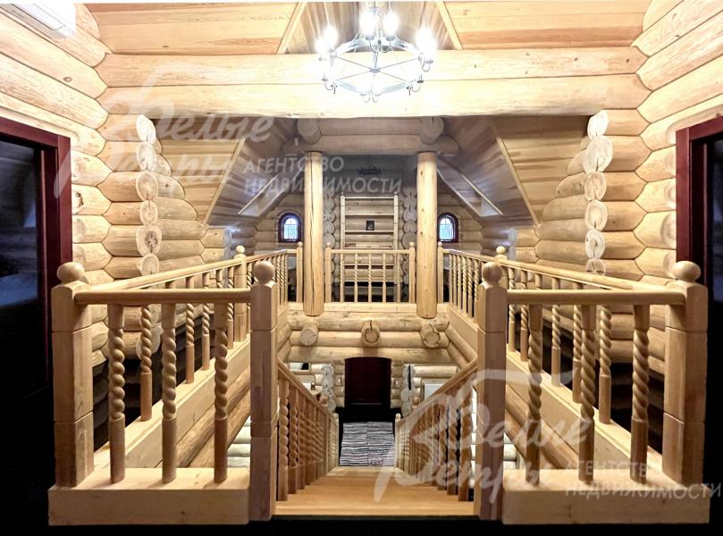 Вид со второго этажа на первый этаж сквозь изящную резную деревянную лестницу