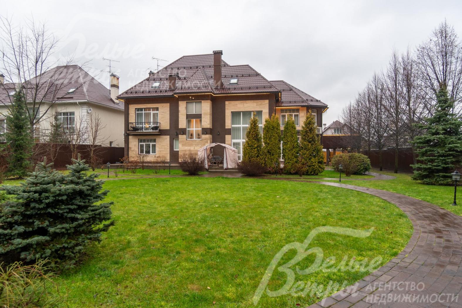 Дом стоит на участке с ландшафтным дизайном с елями и взрослыми деревьями