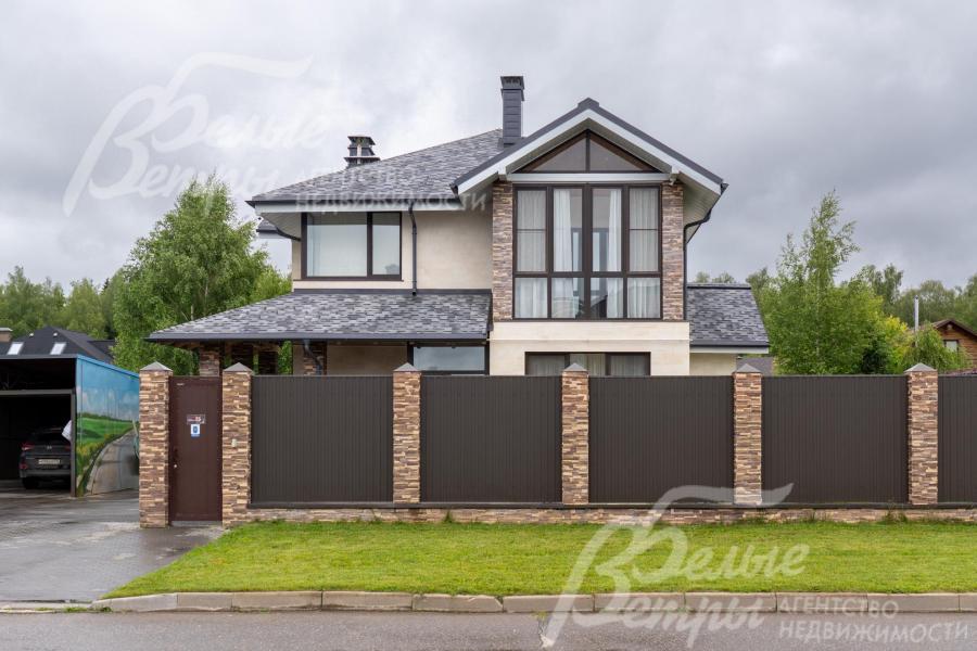 По фасаду дом ограждён забором с каменными столбами, облицованными искусственным камнем в стиле дома