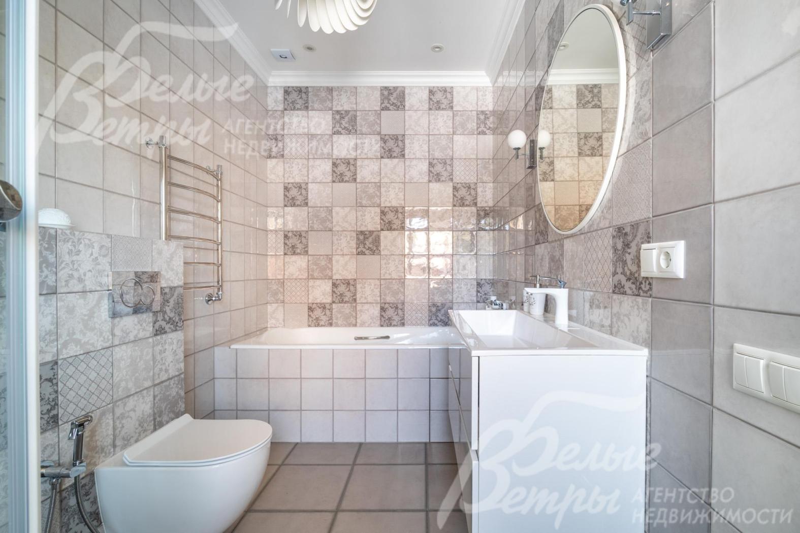 Санузел мастер-спальни с ванной оформлен светлой плиткой с декором