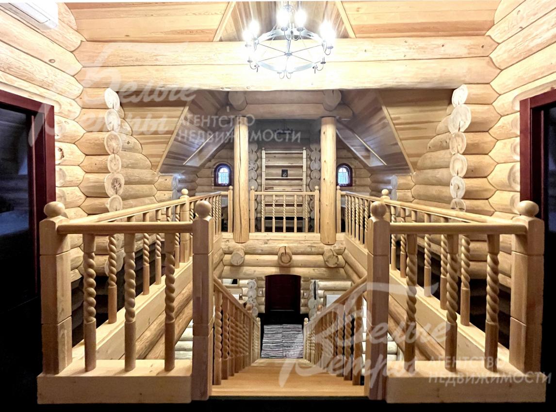 Вид со второго этажа на первый этаж сквозь изящную резную деревянную лестницу