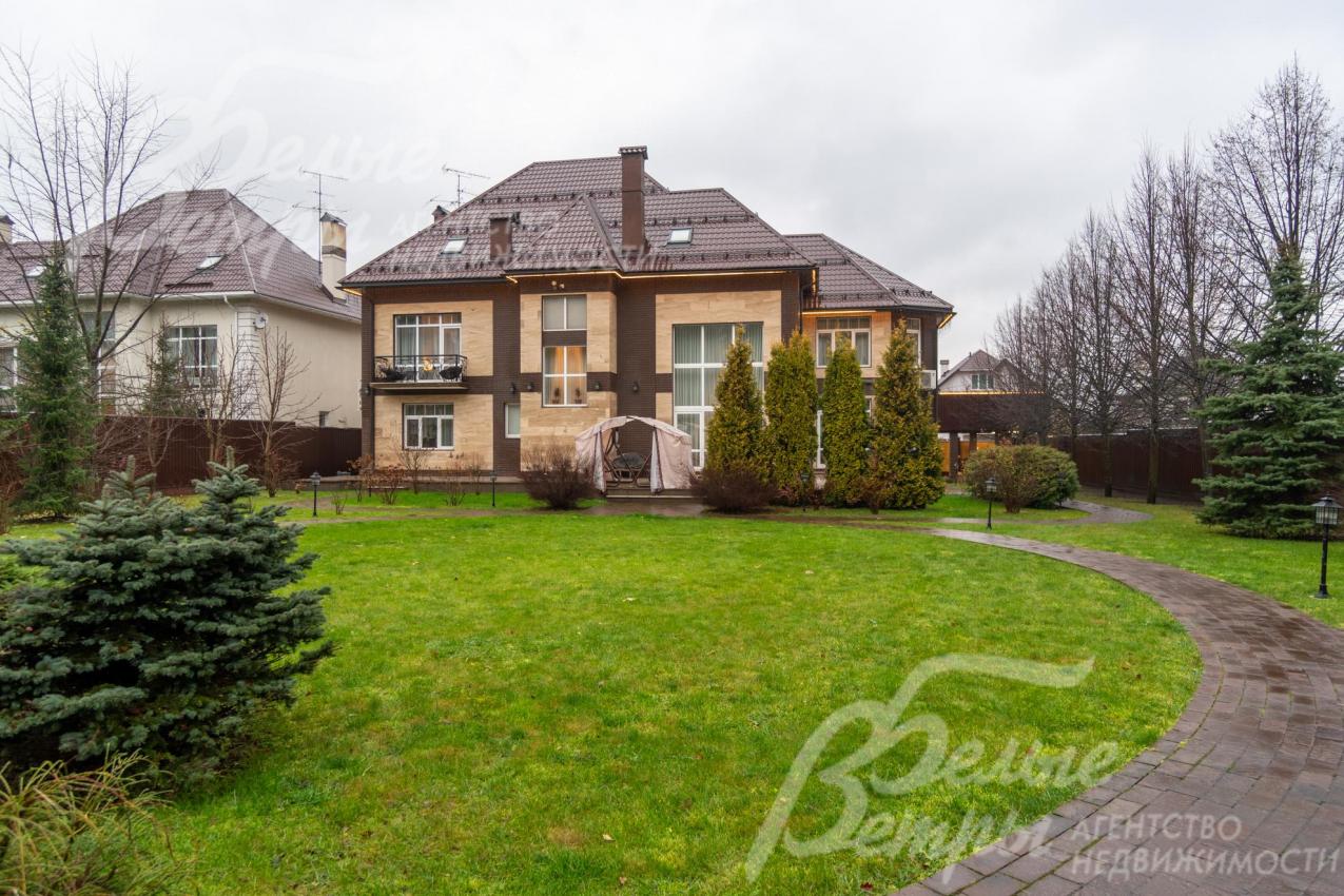 Дом стоит на участке с ландшафтным дизайном с елями и взрослыми деревьями